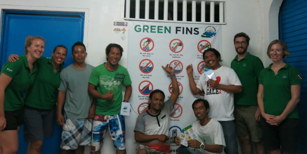 Picture of Green Fins Philippines assessors with members from dive centres in Malapascua. They are pointing at a Green Fins briefing poster. 