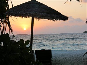 Picture of a sunset over the ocean, with a beach umbrella in the foreground. 