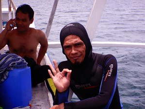 Picture of a diver on the side of a boat making the 'OK' hand gesture. 