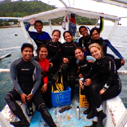 Picture of the Reef-World team with the Green Fins Coordinators in Mabini. They are sitting on a dive boat wearing wetsuits. 