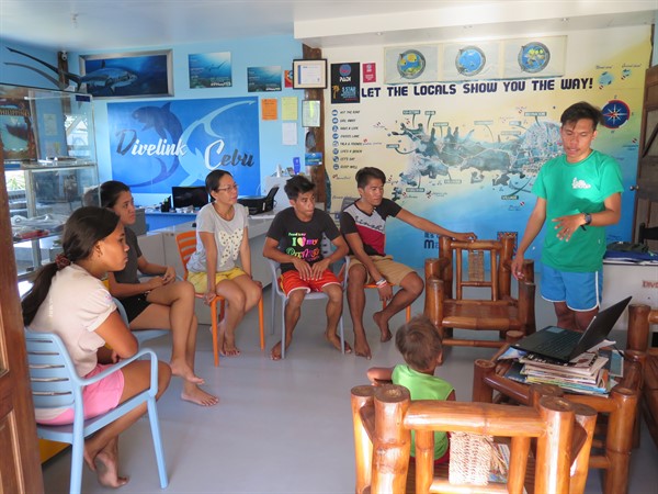 Picture of the Green Fins Philippines team meeting with members at a dive centre. A group of people is sitting around a laptop. 