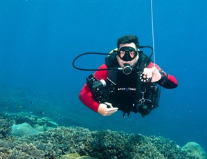 Picture of Rob from Ceningan Divers diving in the ocean holding photographic equipment. 