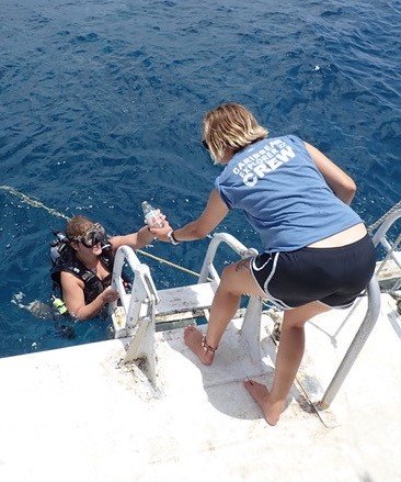 Picture of the Explorer Ventures team returning from an underwater clean-up. A diver is passing trash to a person on a boat. 