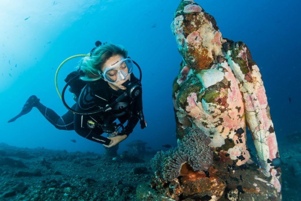 Photo of scuba diver swimming in the ocean with an underwater statue