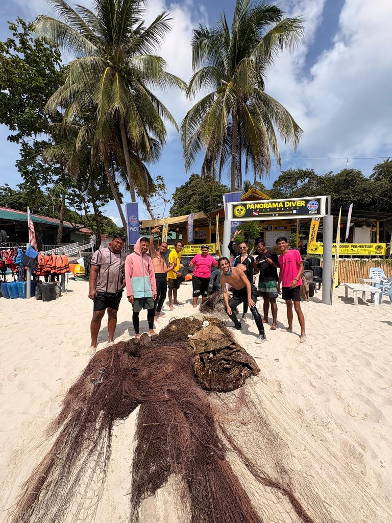 The Panaroma Divers crew standing on a beach in front of the dive shop with a pile of ghost nets in front of them.